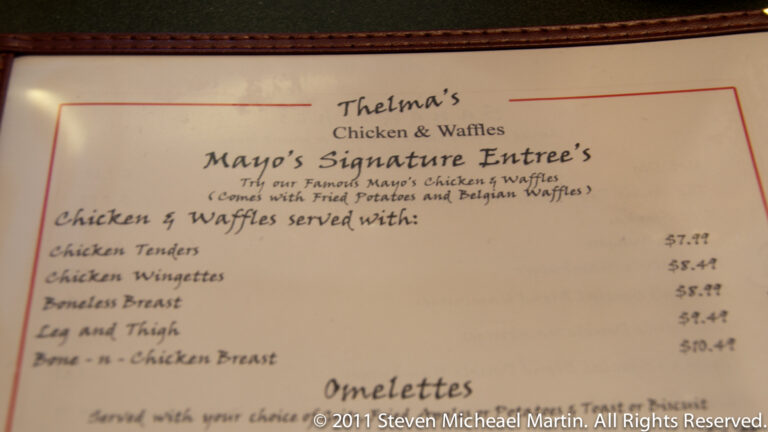 A cream-colored restaurant menu fills the frame, with the heading “Thelma’s Chicken & Waffles” above chicken entrees and omelettes.