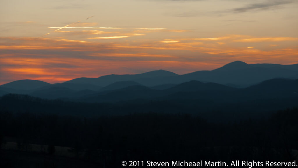 Bright orange clouds and horizon glow behind a dark, jagged line of mountain peaks.