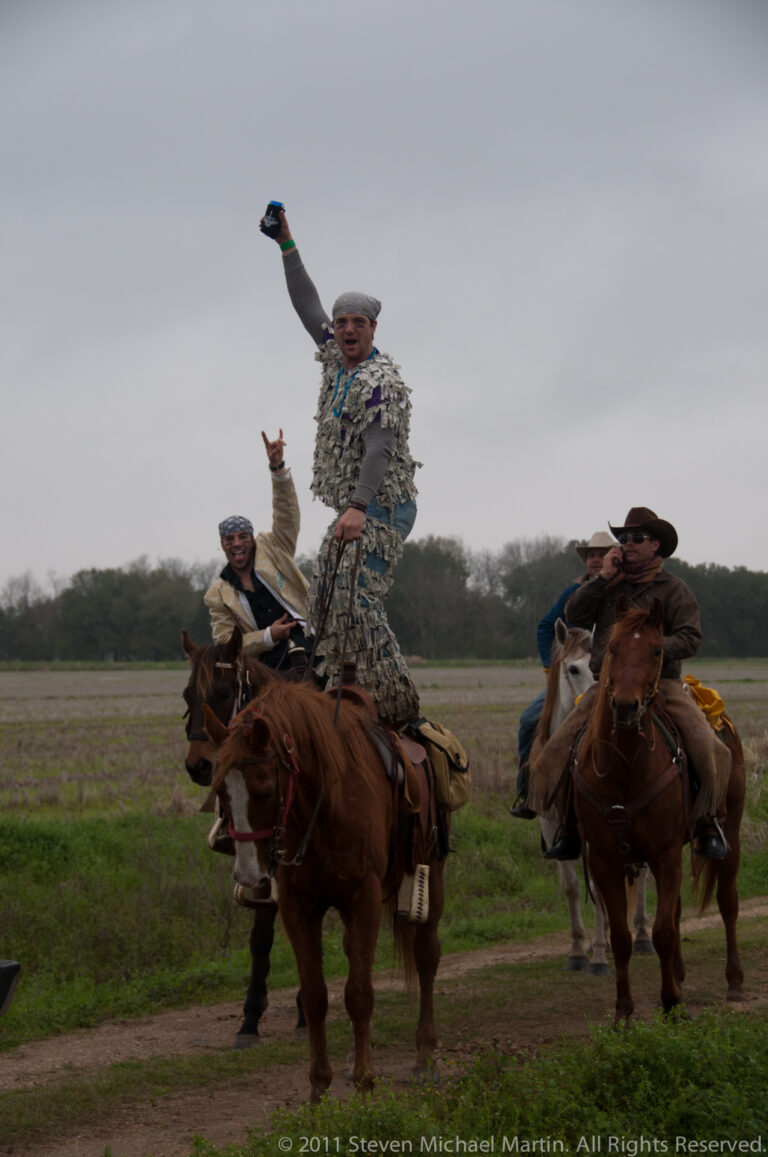 Costumed riders gather on horseback in a wet field as one man raises an arm.