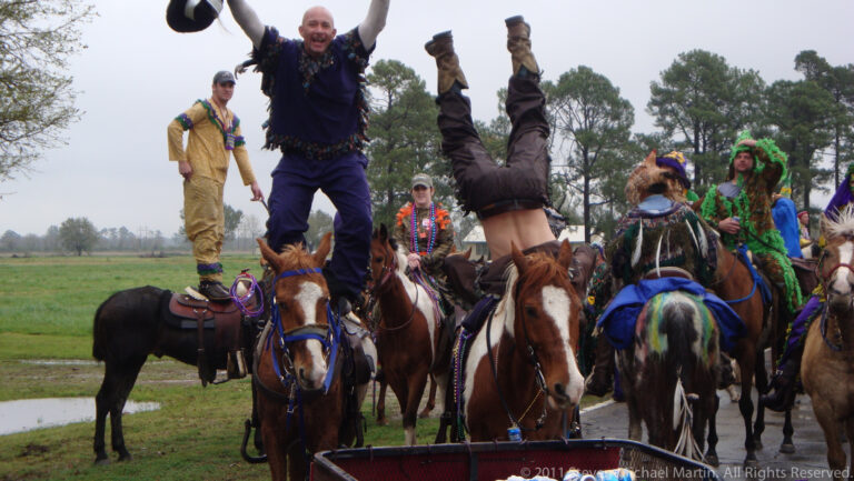 A participant balances upside down above a horse as another man cheers among mounted riders.