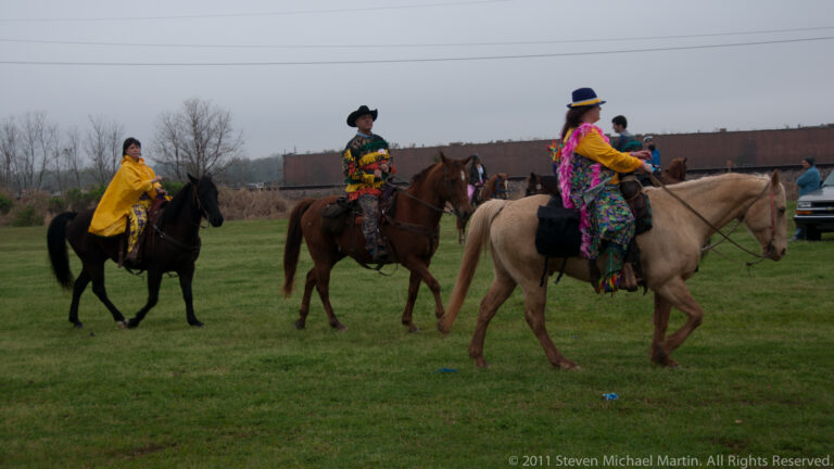 Three costumed riders move across a grassy field in front of a long freight train.