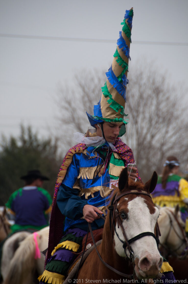 A rider in blue costume and a towering striped hat sits on a brown-and-white horse.