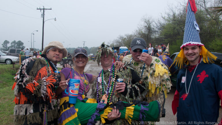 Costumed adults pose together outdoors, holding one participant horizontally across the group.