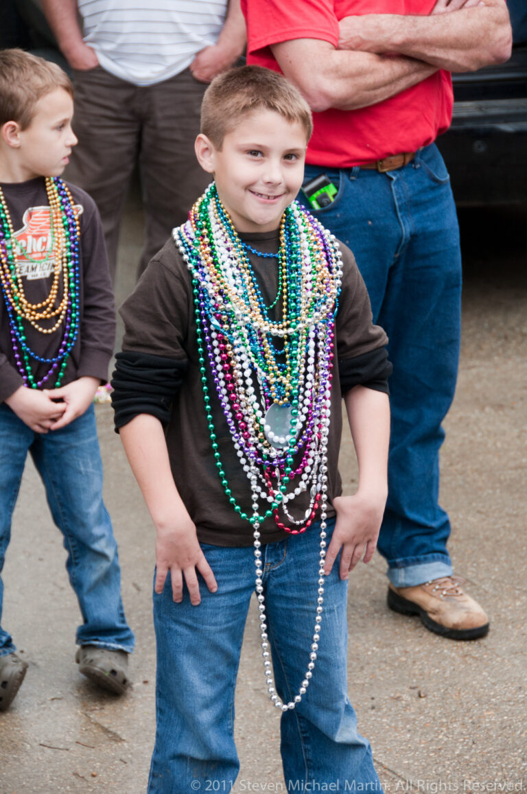 Young boy in a dark sweatshirt and jeans wears many colorful bead necklaces among other festivalgoers.