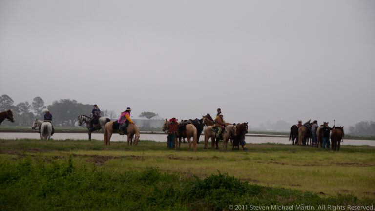 Several costumed riders pause on horses across a misty, flat green pasture.