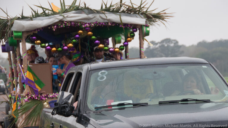 Decorated trailer with passengers follows a gray vehicle marked with a white number eight.