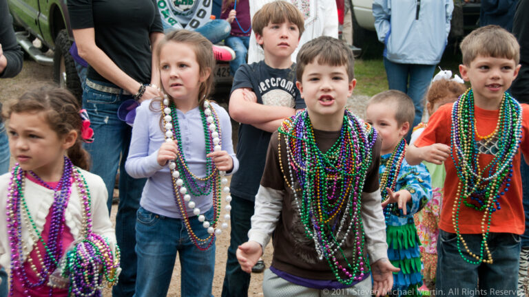 Children wearing colorful bead necklaces stand together in a crowd of adults.