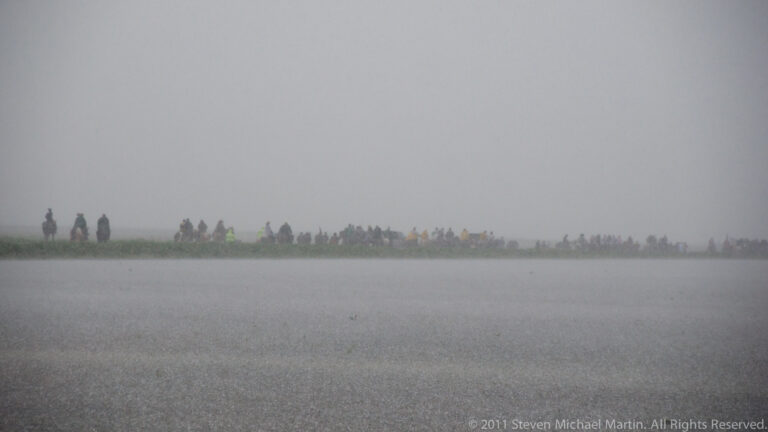 Horseback riders appear as faint silhouettes along the far bank in dense gray fog.