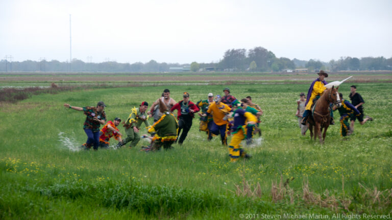 Costumed participants run through a wet field while a horseback rider follows behind.
