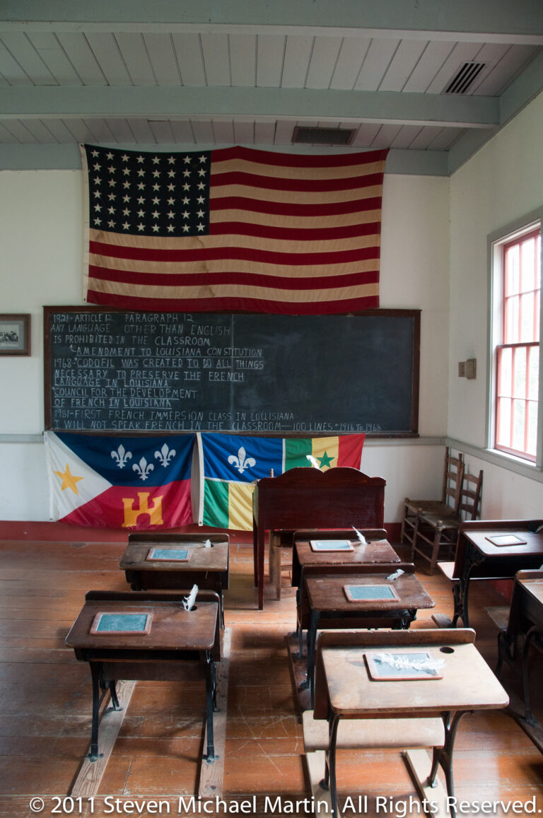 Rows of wooden desks face a chalkboard beneath a United States flag and several colorful banners.