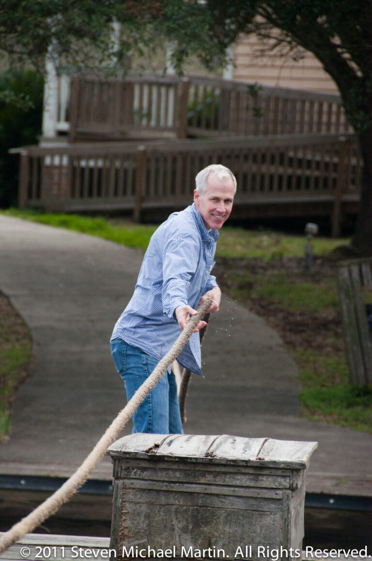 A man braces himself while pulling a rope connected to a weathered wooden well structure.
