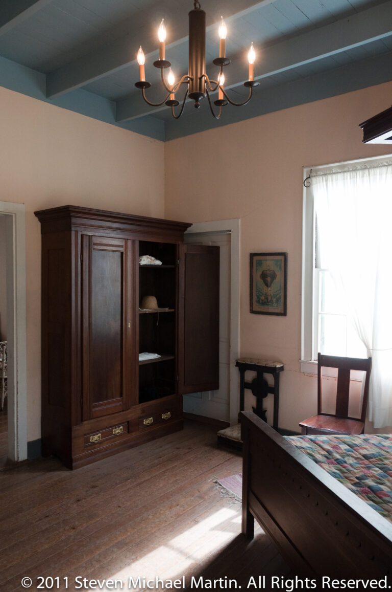 A dark built-in cupboard faces a partly visible dining table as sunlight falls across the plank floor.