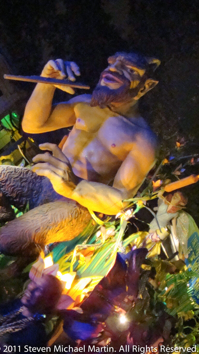 Blurred gold and purple sculptural forms pass above a green-lit float base at night.
