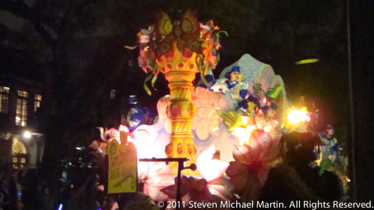 Costumed figures surround a tall glowing gold-and-red crown-shaped structure on a night float.