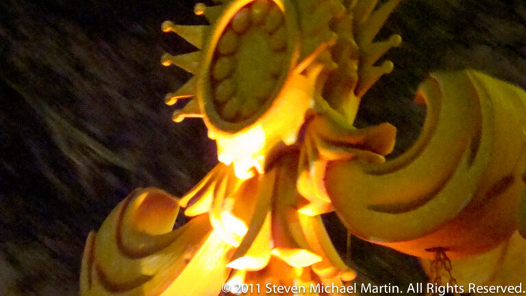 Orange and yellow oversized faces cluster together on a brightly lit nighttime float.