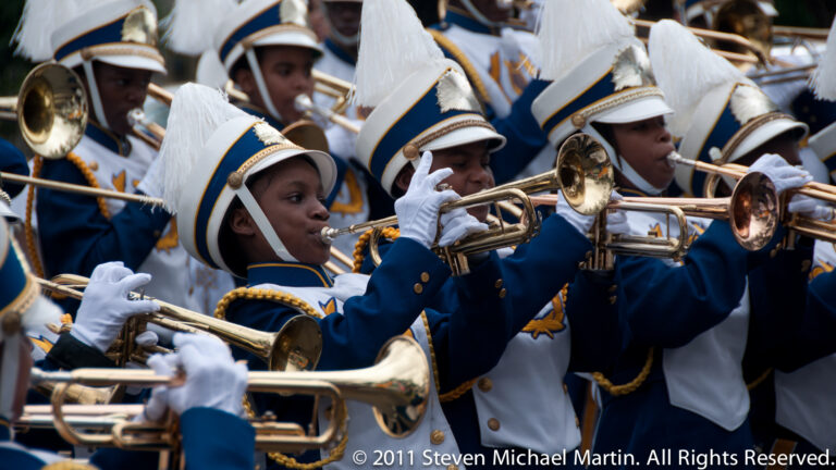 Young musicians in navy-and-white uniforms play trumpets and trombones in a parade band.