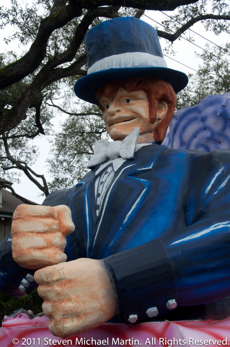 An oversized Uncle Sam figure in a blue suit and striped trousers reaches forward from a float.