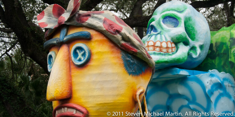 A yellow-orange face with blue eyes sits in front of a green-and-white skull-like figure.