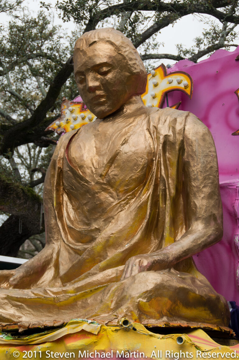 A gold-colored seated figure is framed by ornate curling decorations on a float.