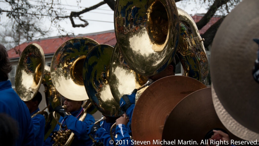 A polished sousaphone fills the foreground as blue-uniformed musicians march behind it.