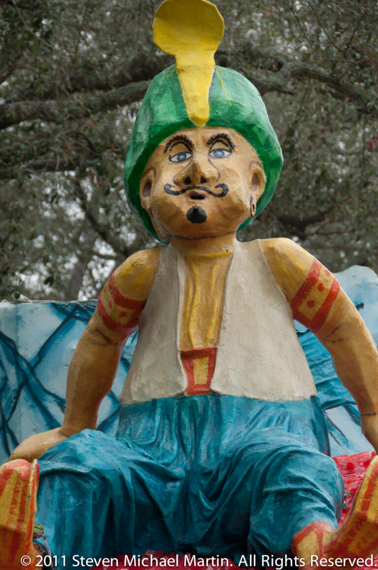 A mustached figure in a green cap and yellow plume wears a pale shirt and blue costume.