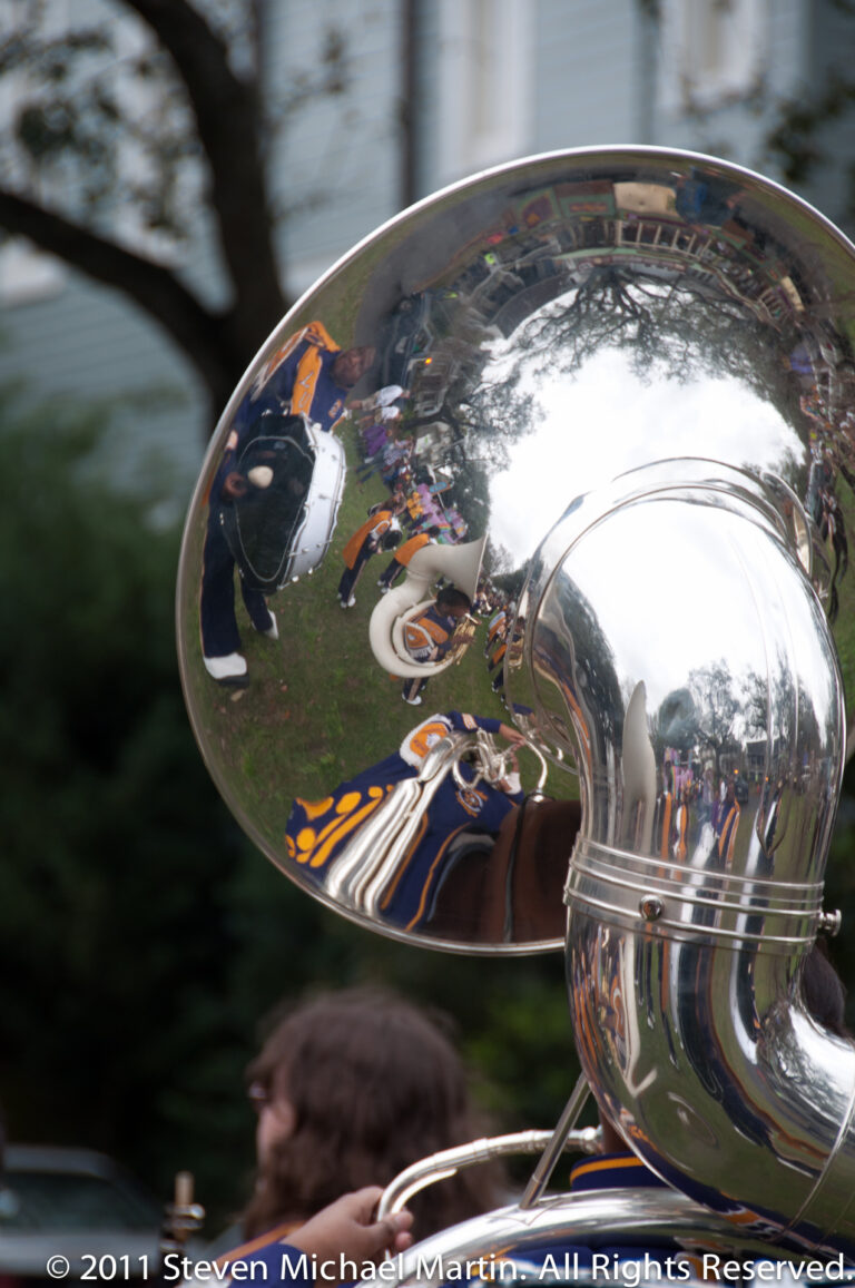 A polished sousaphone bell reflects distorted spectators and parade activity.