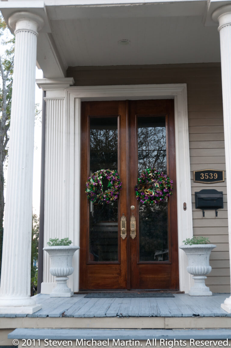 A double wooden door marked 3539 is framed by white columns, flower arrangements, and urn planters.