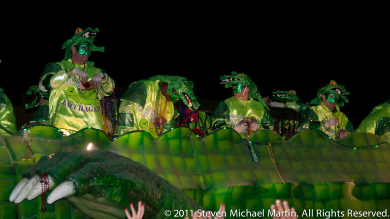 Green-costumed riders stand above the scaled body and clawed feet of an alligator float at night.
