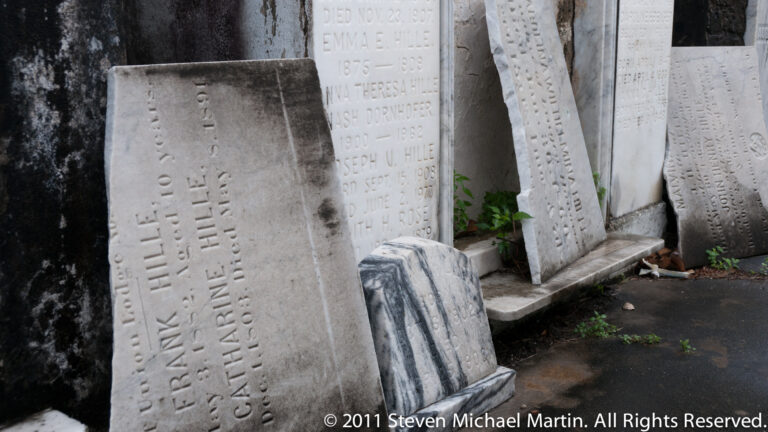 Upright marble grave tablets with engraved names and dates stand closely together in a New Orleans cemetery.