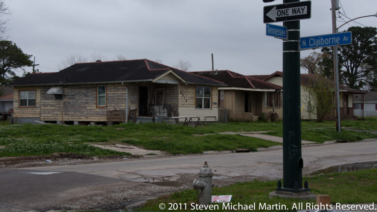 Street signs for Tennessee Street and North Claiborne Avenue stand above a fire hydrant and modest houses.
