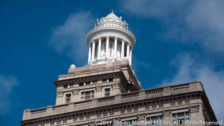 A columned circular cupola crowns a stone office building against a deep blue sky.