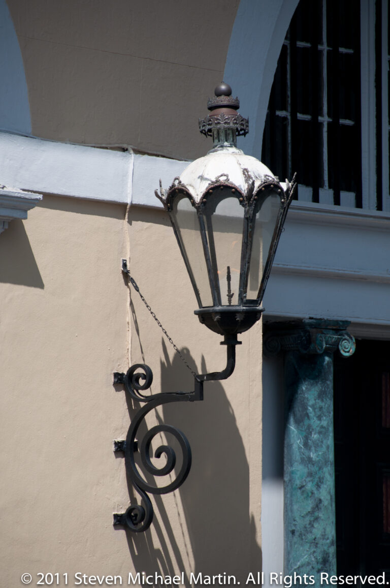 An ornate metal lantern with a curled bracket projects from a pale wall beside a dark window.