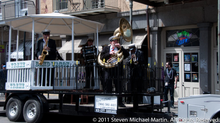 Brass musicians perform on a raised trailer platform beside a storefront and street.