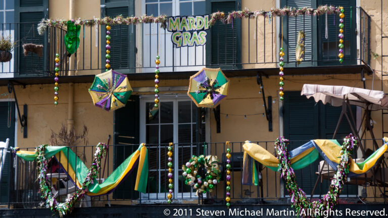 Mardi Gras umbrellas, beads, and streamers decorate a French Quarter balcony above shuttered windows.
