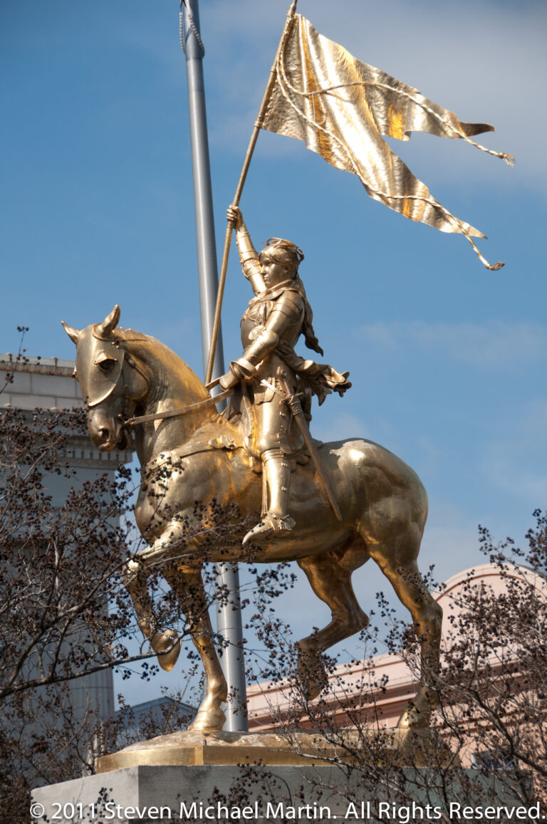 A gilded armored rider on a rearing horse holds a banner above a low roofline.