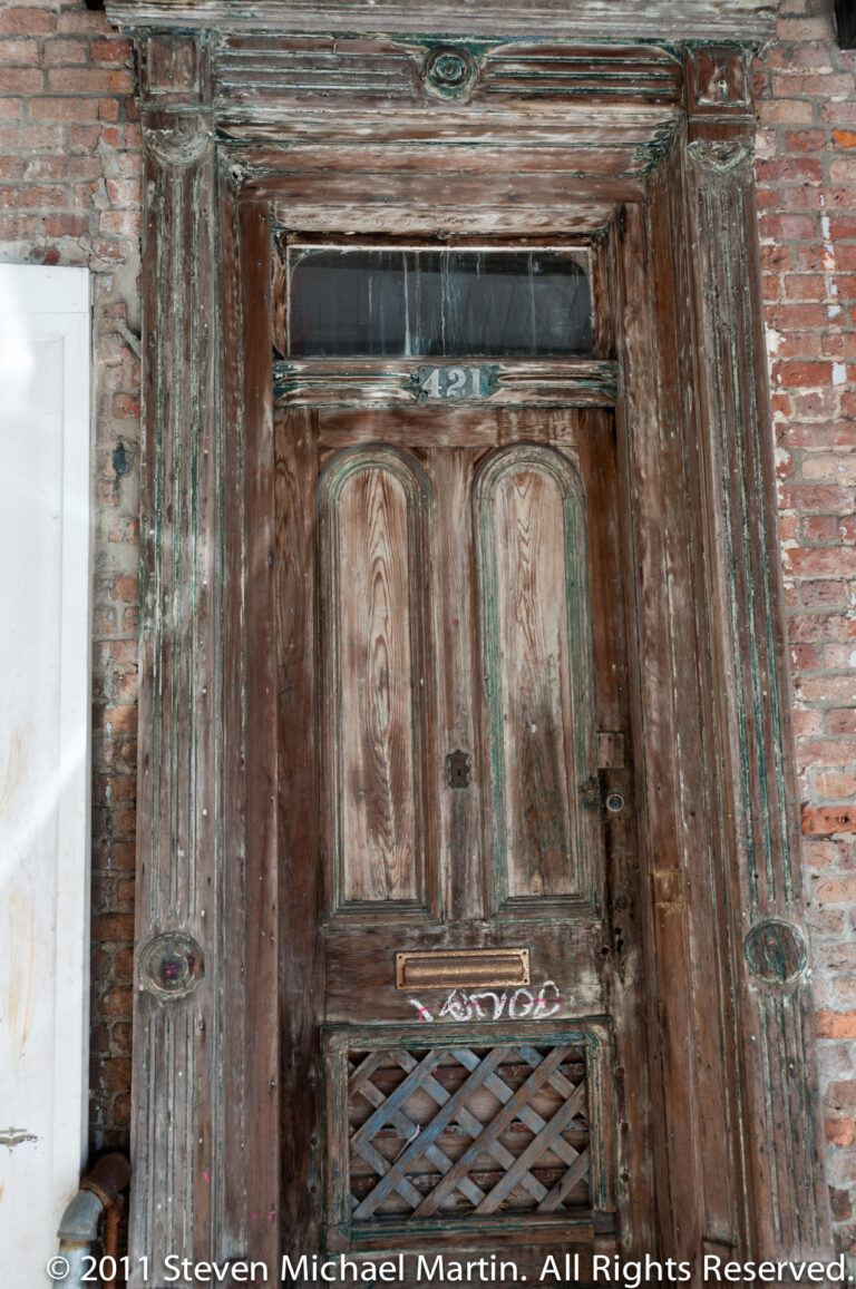 A weathered double wooden door marked 421 sits within a brick-and-plaster entrance.