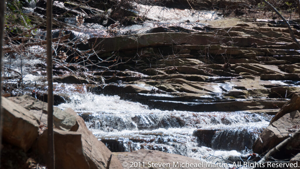 Water cascades over layered stone shelves beneath thin branches.