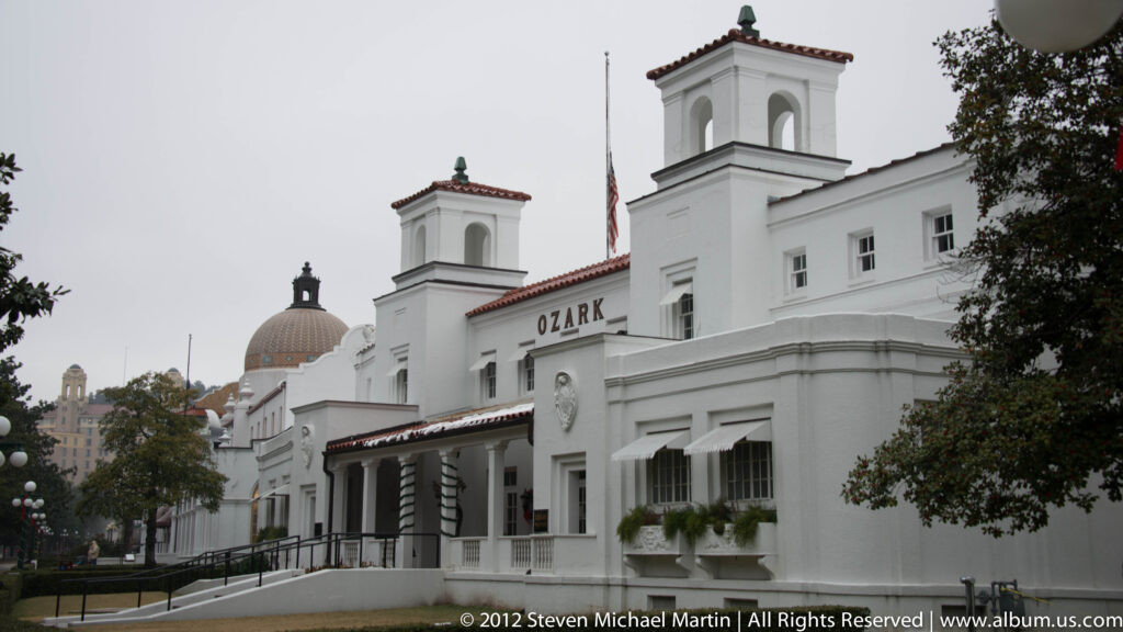 The white Ozark Bathhouse has twin towers, a long entrance portico, and a dome behind the roofline.