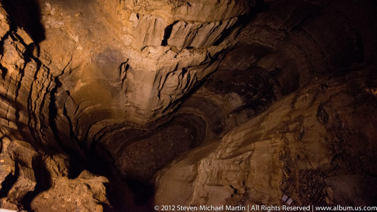 Amber light reveals horizontal layers and irregular fractures across a limestone cave wall.
