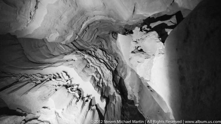 Pale rippled mineral layers cover a steep cave wall, their ridges outlined by dark seams.