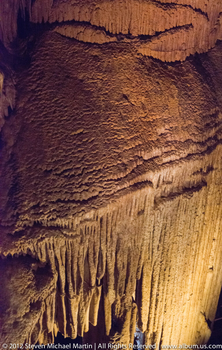 Fine mineral ridges fringe a ledge beneath thin horizontal bands on a warmly lit cave wall.