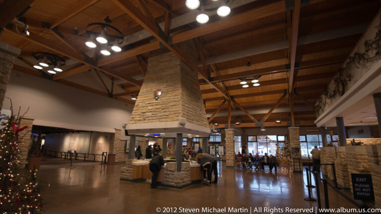 Visitors stand in a lobby with timber roof trusses, stone columns, counters, and a decorated tree.