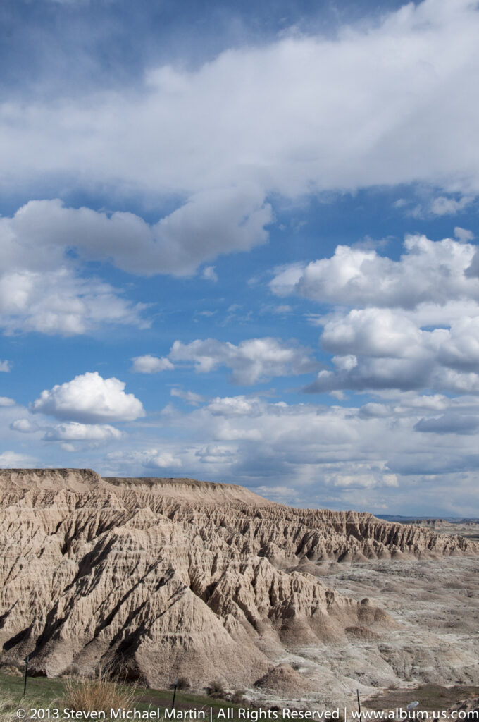 A wide panorama of pale badlands ridges extends beneath a sky of broken white clouds.