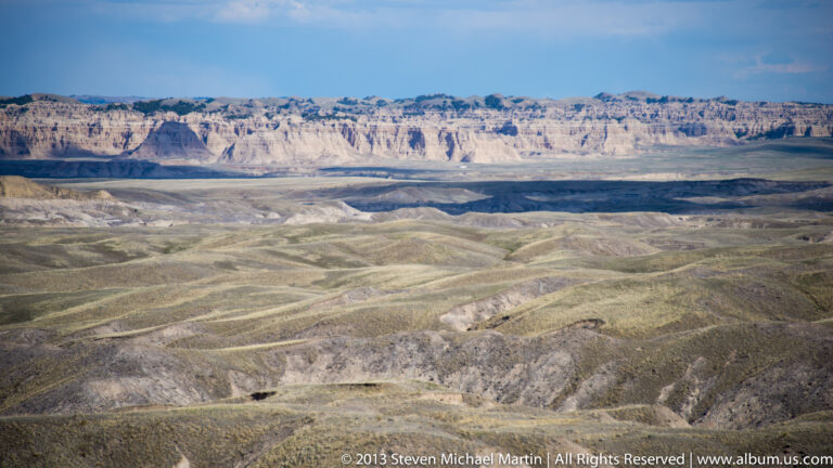 A broad basin of pale ridges and shallow channels leads toward a long distant escarpment.