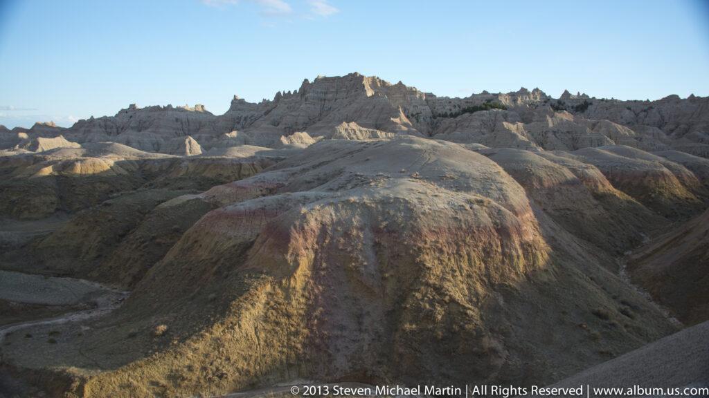 Warm evening light falls across ridges and gullies, with a rounded mound in the foreground.