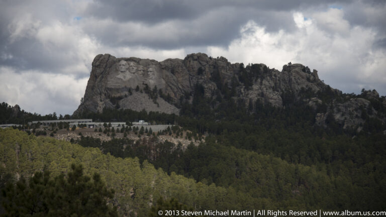 Four carved presidential faces rise above a pine-covered slope beneath heavy clouds.