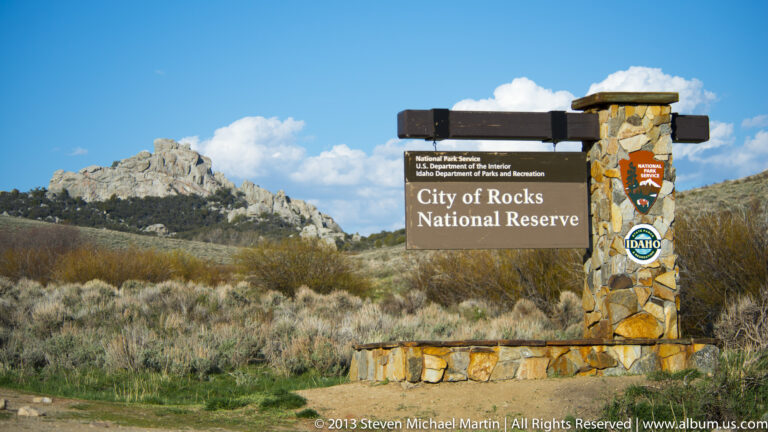 A stone entrance sign reading City of Rocks National Reserve stands before a rocky ridge.