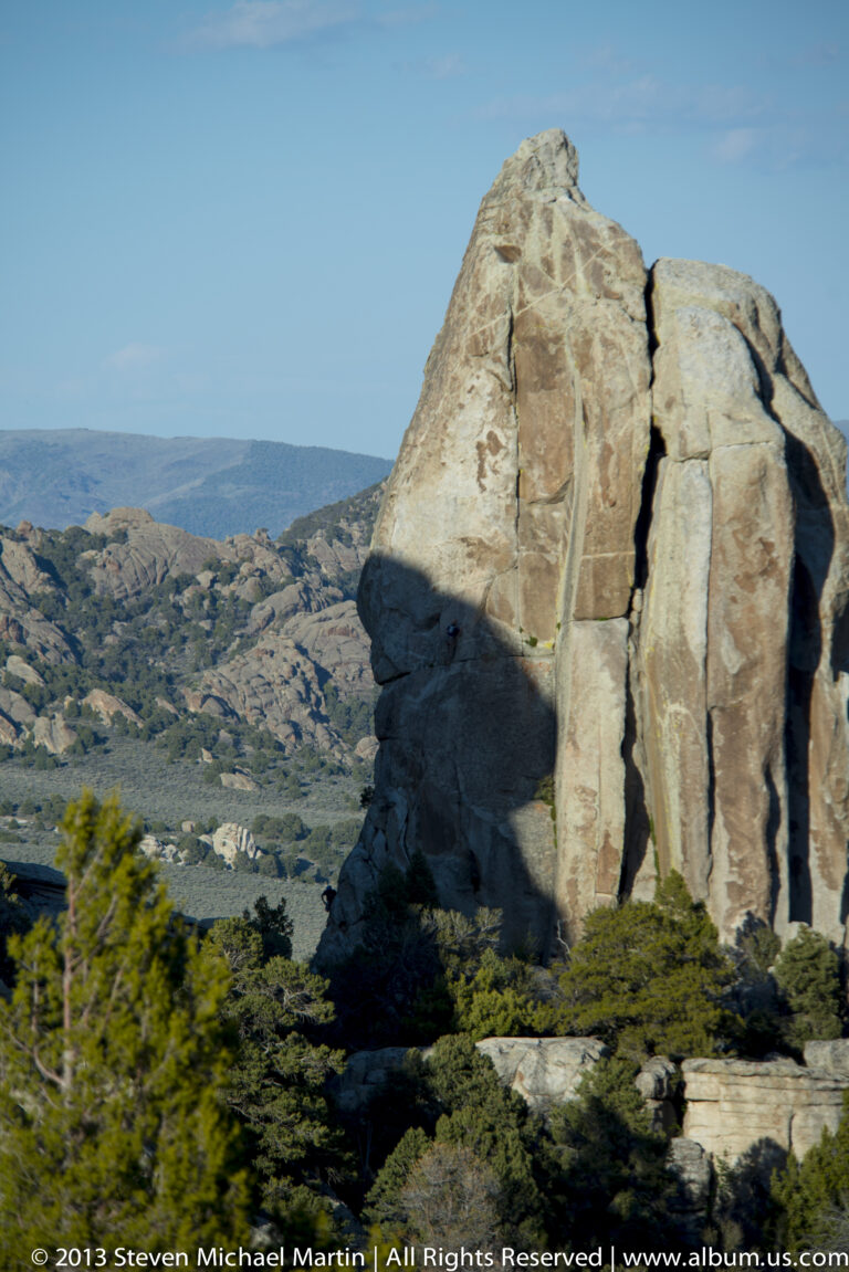 A tall sunlit granite outcrop rises above wooded hills and a distant valley.