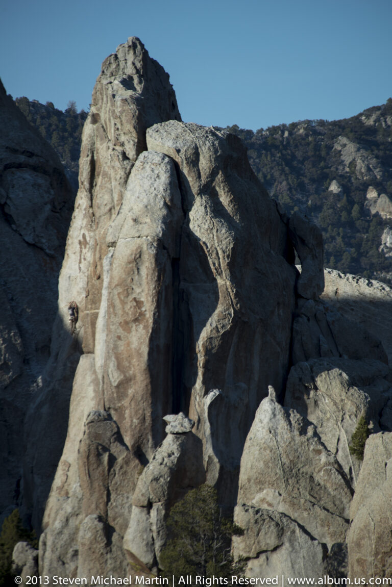 A sunlit granite slab stands among shadowed boulders below a wooded ridge.