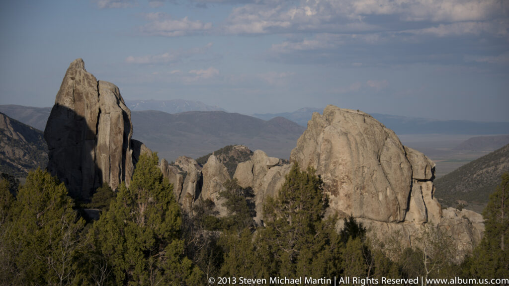 Two pointed granite towers rise above evergreens against hazy distant mountains.